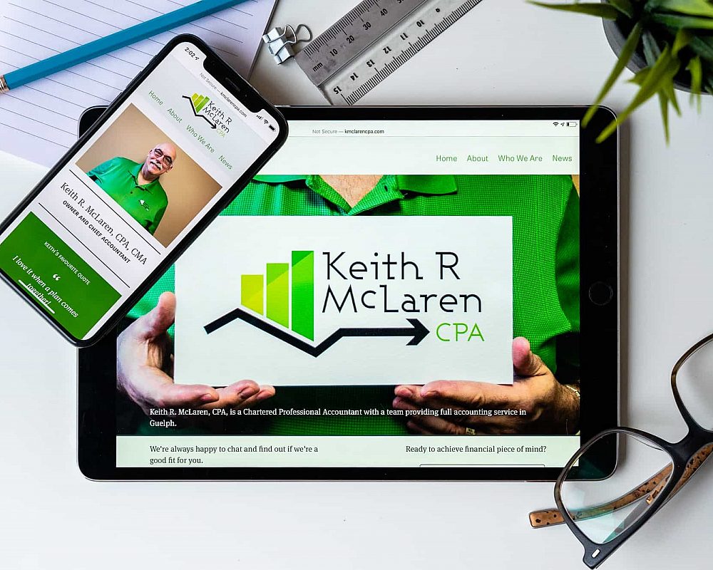 The Keith McLaren website on a tablet and a smartphone with glasses and other desk apparel nearby